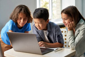 diverse happy school kids using laptop computer together in classroom.