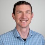 Alt text: Smiling professional man in checkered shirt, expert in educational technology.