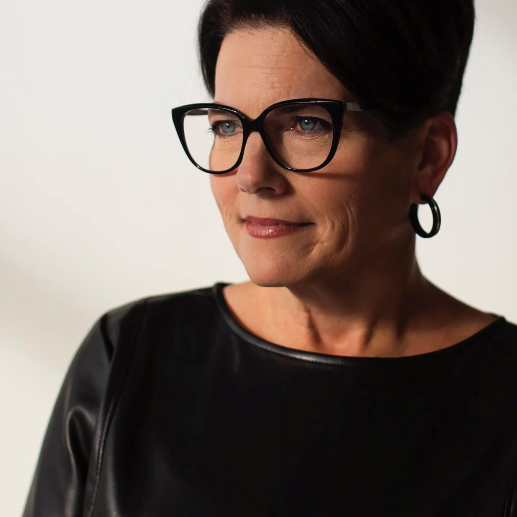 A photo of a woman with short, dark hair and glasses smiling to the side