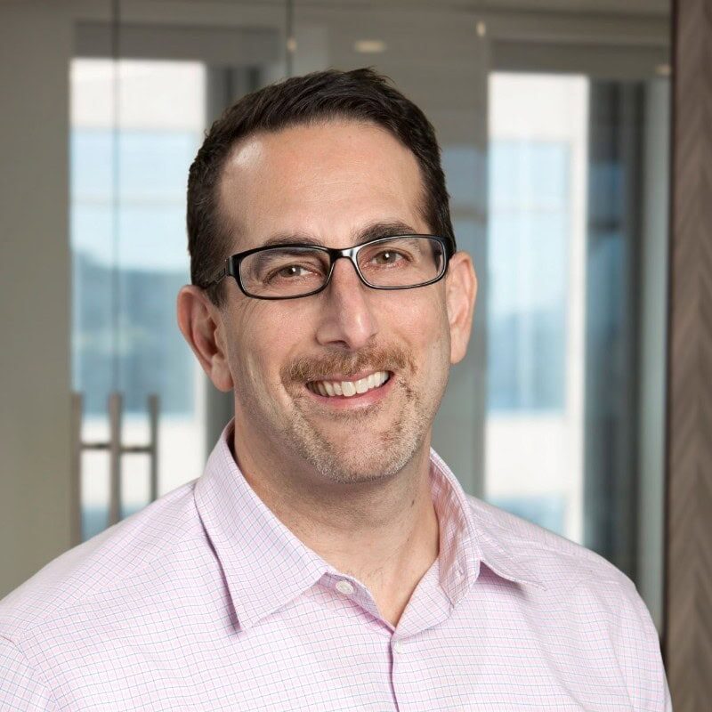A profile photo of a man with glasses smiling towards at you.
