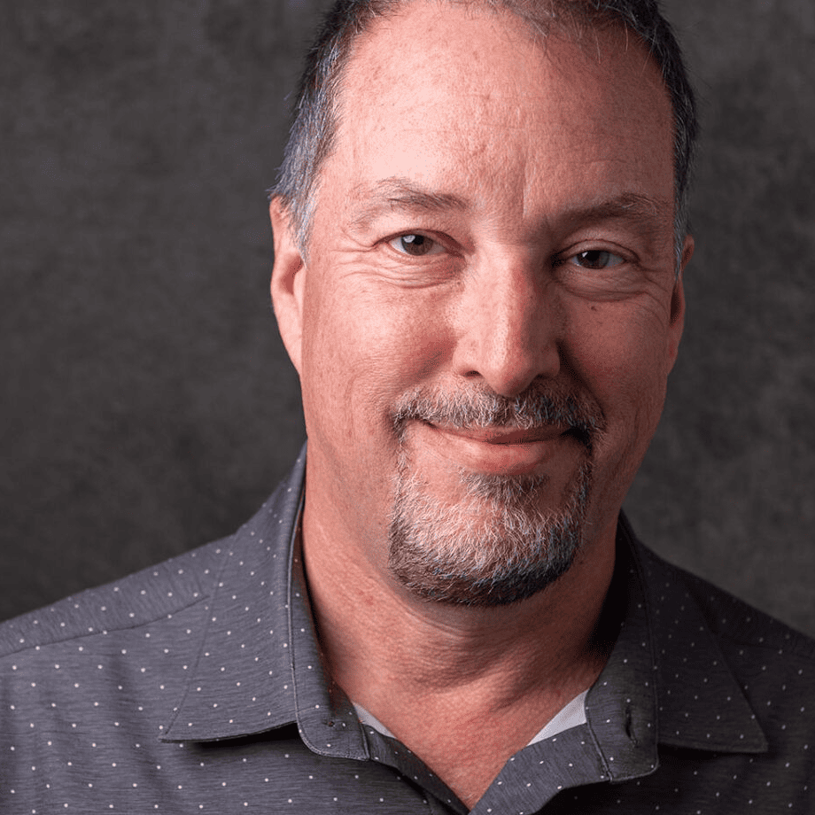 A headshot-style photo of a man smiling at you